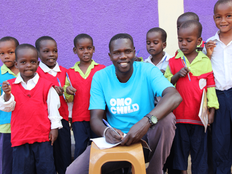 A man wearing an Omo Child shirt sitting with young children.