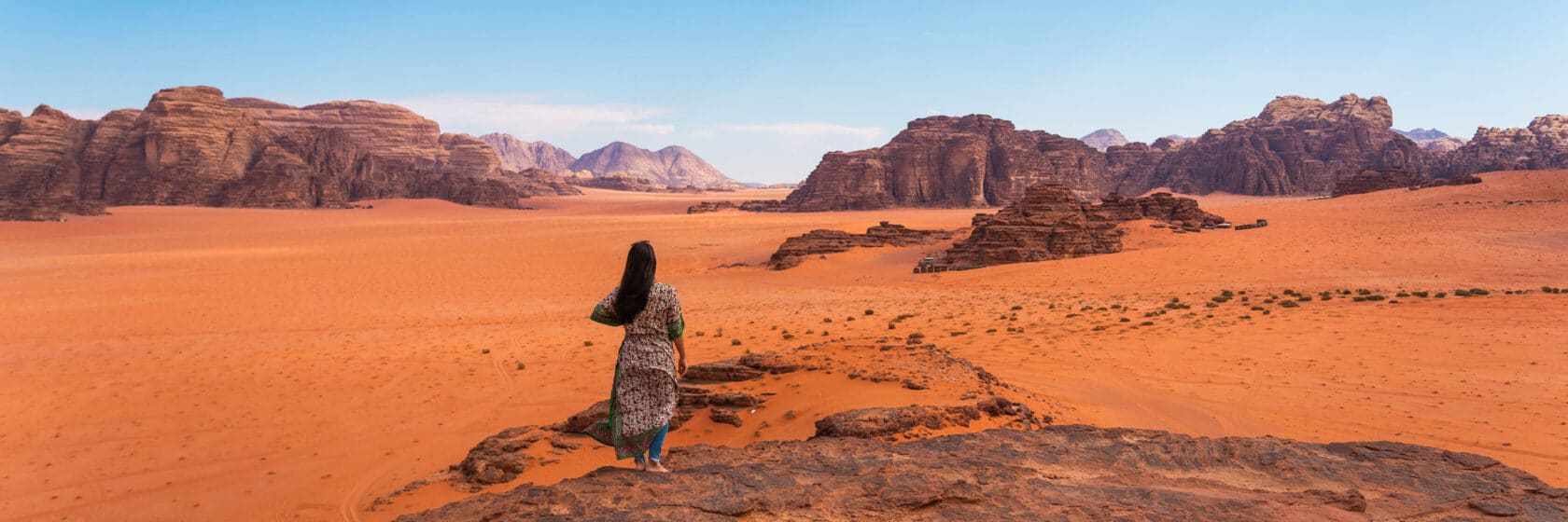 A tourist dressed in a local Arab dress standing on top of mountain and enjoying landscape of Wadi Rum desert in Jordan.