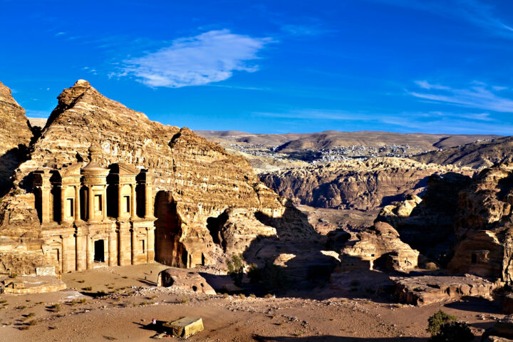 Ancient rock-carved monastery in Petra, Jordan, situated amongst rugged desert mountains under a clear blue sky, reminiscent of a real-life Indiana Jones adventure.