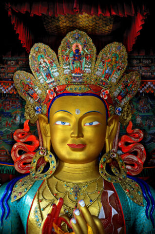 A golden statue of a Buddhistic deity with an ornate, colorful crown and intricate detailing, situated in a richly decorated temple that feels like a glimpse into Shangri-La.