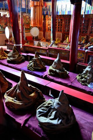 Rows of conical cloth-covered objects line long benches in an interior space, reminiscent of a hidden Shangri-La, featuring colorful decor and wooden pillars.
