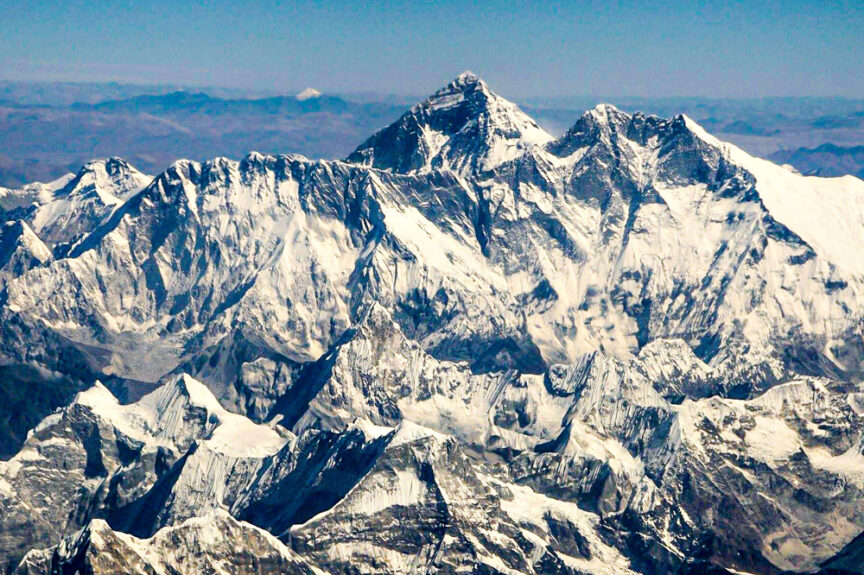 Aerial view of the snow-covered Mount Everest and surrounding peaks rising majestically above the clouds under a clear blue sky.