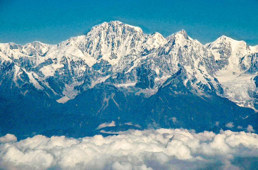 Snow-capped mountain peaks rise majestically above the clouds, with a bright blue sky in the background.