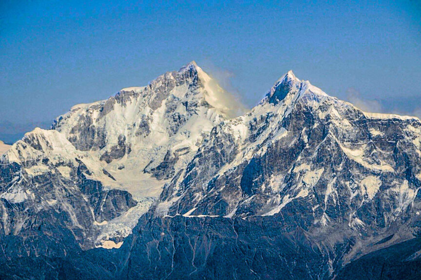 Snow-covered mountain peaks rise above the clouds under a clear blue sky.