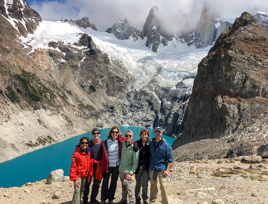 A group of six people pose for a photo in front of a dramatic mountain landscape with a glacier and turquoise lake in the background, capturing the essence of Patagonia's wilds.