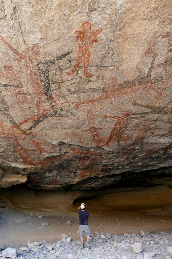 Person photographing ancient rock paintings on a cave wall, capturing depictions of human figures and animals, as if going back in time.