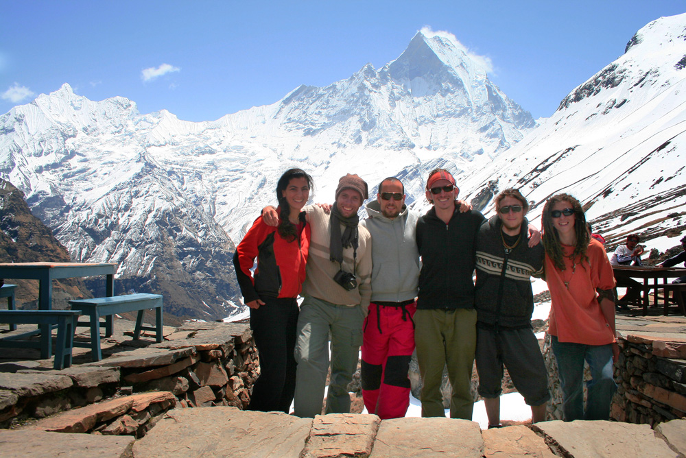 Six people standing together on a snowy mountain trail in Nepal, with a snow-covered peak in the background, capturing a perfect moment for a family photobook.
