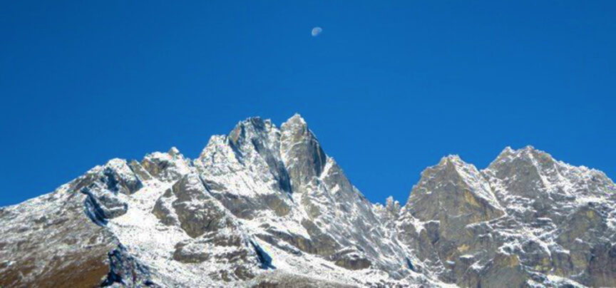 Snow-covered mountain peaks under a clear blue sky with the moon visible, invoking a serene hum of tranquility.