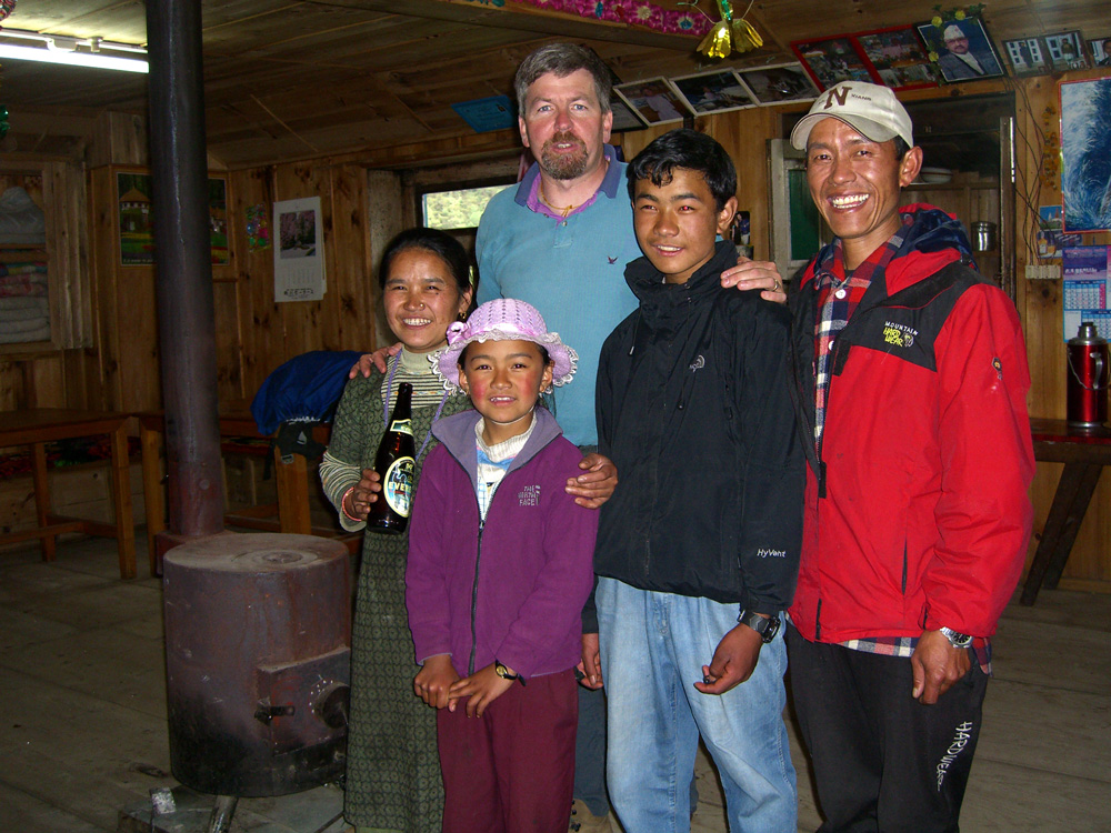 A group of five people, four men and two women, pose together inside a wooden room with a stove, capturing a precious moment for their family photobook in Nepal.