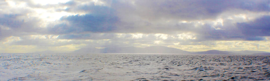 A calm sea under a cloudy sky with distant mountains on the horizon, offering a Céad Míle Fáilte to all who behold its serene beauty.