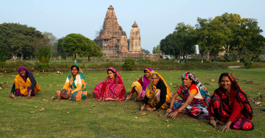 A group of women in colorful clothing sit on grass with ancient temple structures in the background, capturing a moment that epitomizes the rich tapestry of the Country of Contrasts.