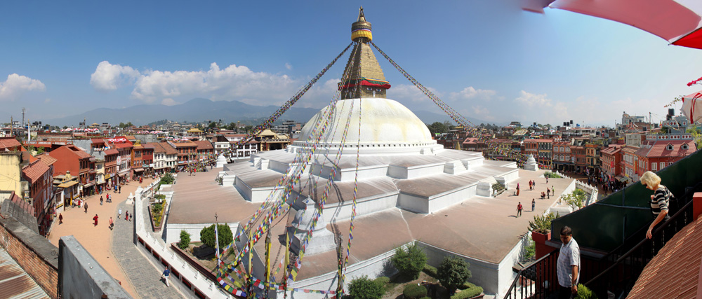 Panoramic view of the Boudhanath Stupa, a white dome with a golden spire, surrounded by buildings and colorful prayer flags in Kathmandu, Nepal—a perfect addition to any family photobook.