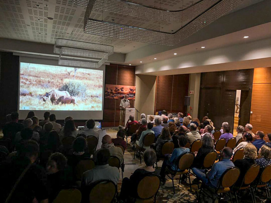 A group of wildlife conservationists seated in a conference room in Namibia watch a special event presentation featuring stunning wildlife images on a large screen.