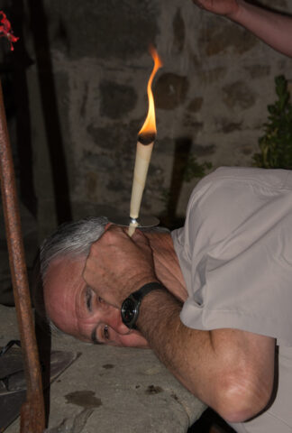 A man with gray hair is lying on his side with a lit ear candling cone inserted in his ear, perhaps dreaming of an adventure in the Apennines.