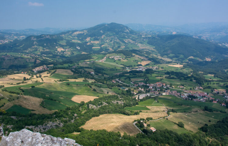 Aerial view of a picturesque landscape with rolling green hills, farmland, and scattered villages under a clear sky, offering an adventure through the stunning Apennines.