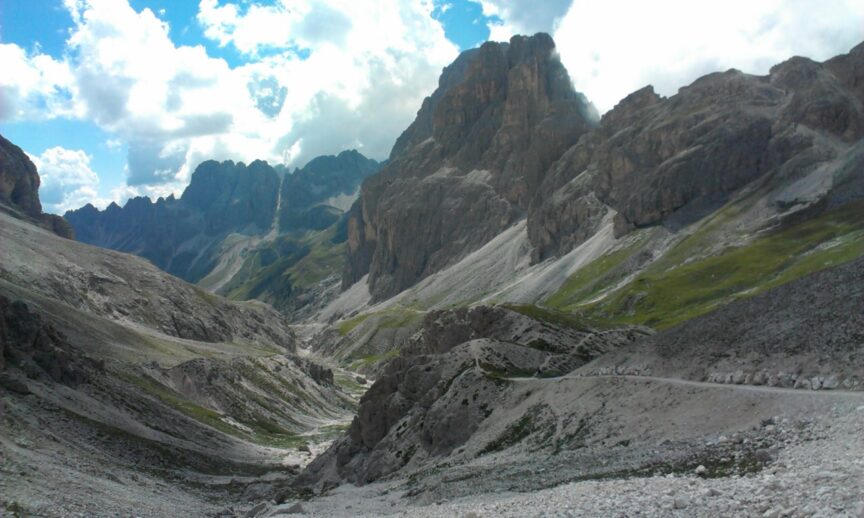 A rugged mountainous landscape with jagged rock formations, sparse greenery, and a partly cloudy sky above. On the Trail With Tania, this adventure scene is devoid of any human presence.