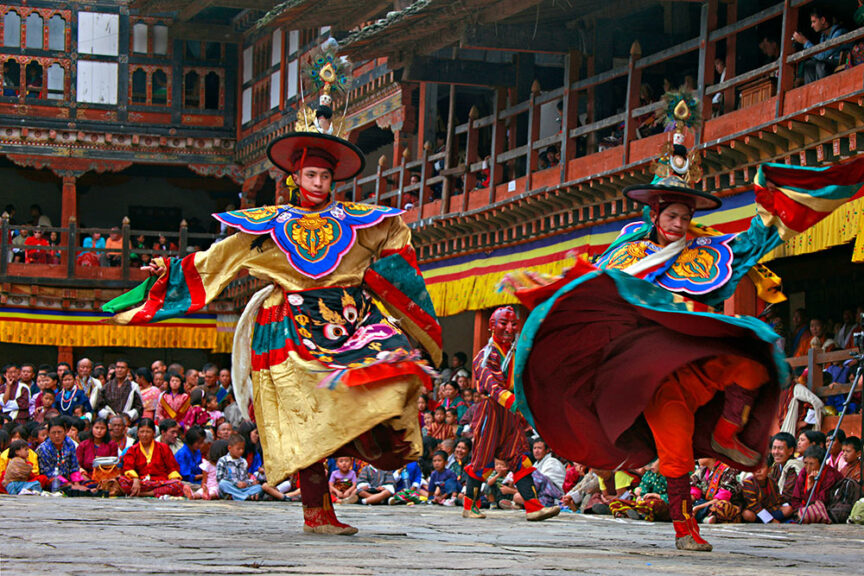 Two individuals in traditional colorful attire perform a lively dance in front of a captivated audience in a courtyard with traditional architectural elements, celebrating one of the amazing festivals from around the world.