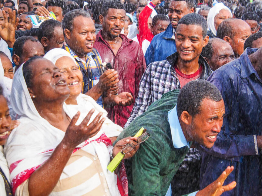A group of people stand closely together, some smiling and raising their hands, while others look ahead, capturing the vibrant spirit of colorful Ethiopia.
