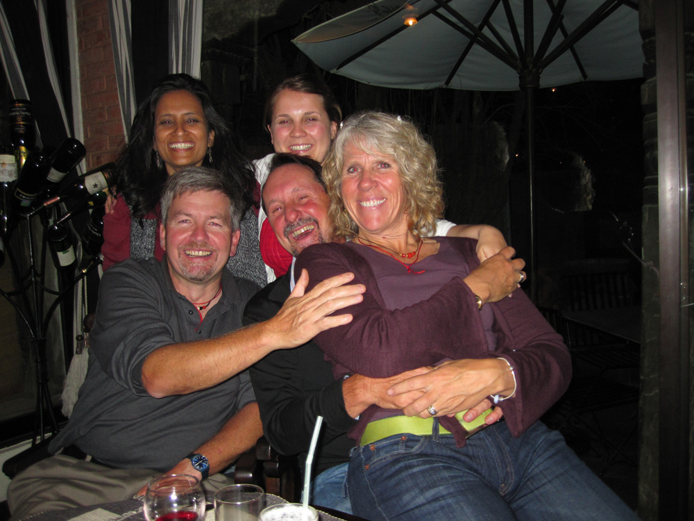 Five family members are posing together and smiling in an outdoor café setting at night, with two sitting and three standing behind them, capturing a moment perfect for their Nepal photobook.