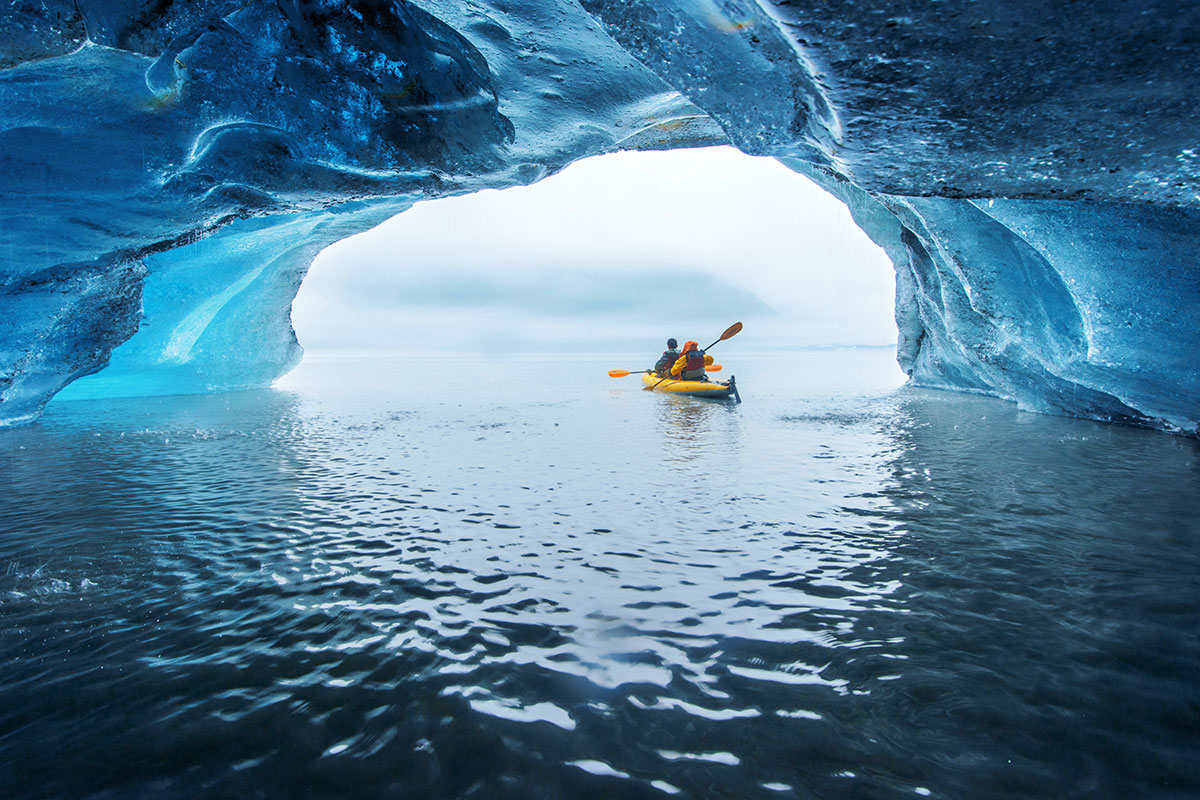 Two people in a yellow kayak paddle through an icy tunnel, emerging into a wide open body of water. This unforgettable experience highlights the awe-inspiring beauty of Alaska's Inside Passage and is a must for any travel enthusiast.