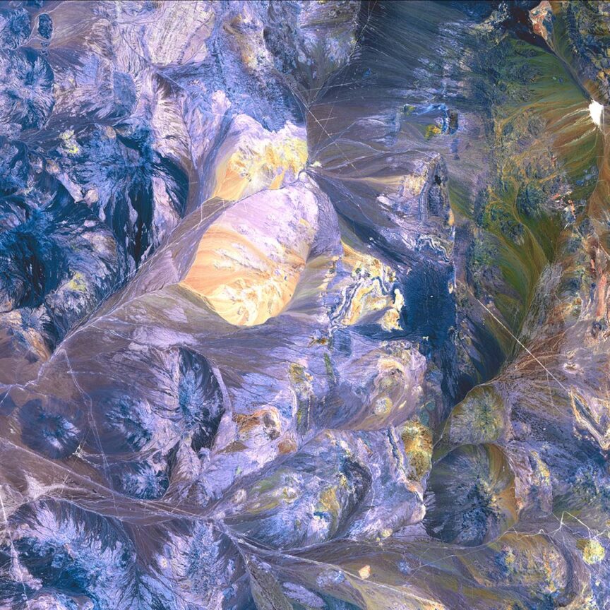 Aerial view of a colorful, abstract, mountainous landscape with prominent hues of purple, green, and yellowish-white patterns; this stunning scene resembles satellite images capturing the Earth's natural beauty.