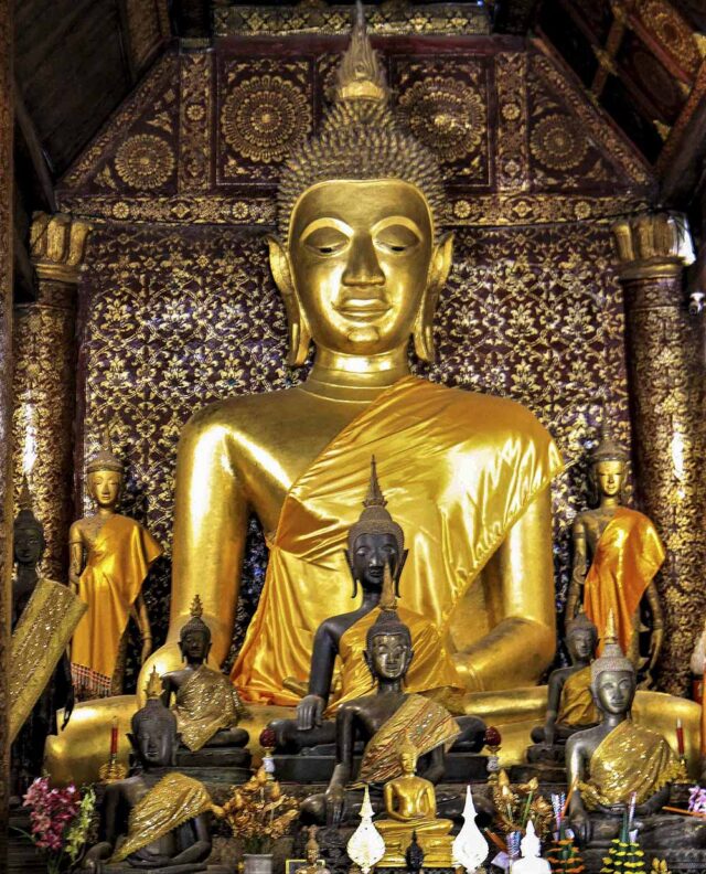 The temple features a large golden Buddha statue surrounded by smaller Buddha figures, set against an ornate, gold-accented backdrop, embodying the spirit of Five Hundred Smiles.