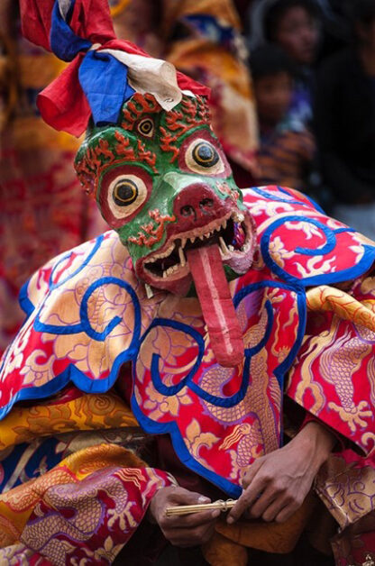 Person wearing a colorful, elaborate costume and a green, ornate dragon mask with a long red tongue and wide eyes during the vibrant Tiji Festival in Nepal.