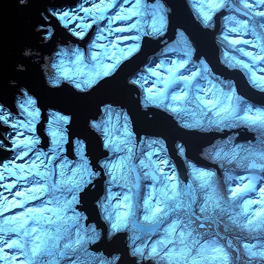 Stunning satellite image of snow-covered mountainous terrain with fjords and dark waterways cutting through the Earth's landscape.