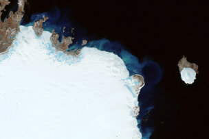 Stunning satellite image showing the northern coast and ice-covered terrain of Greenland with surrounding dark ocean waters and a smaller ice-covered island nearby on Earth.