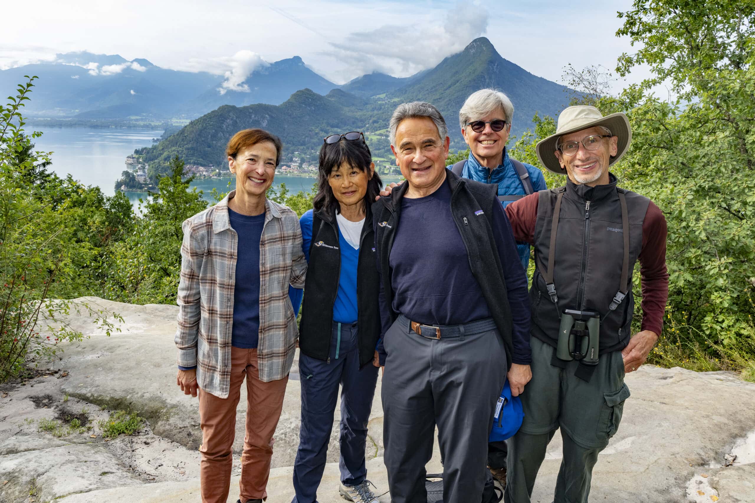 Five people posing on a rocky area with a scenic view of mountains and a lake in the background, capturing the essence of an autumn hike.