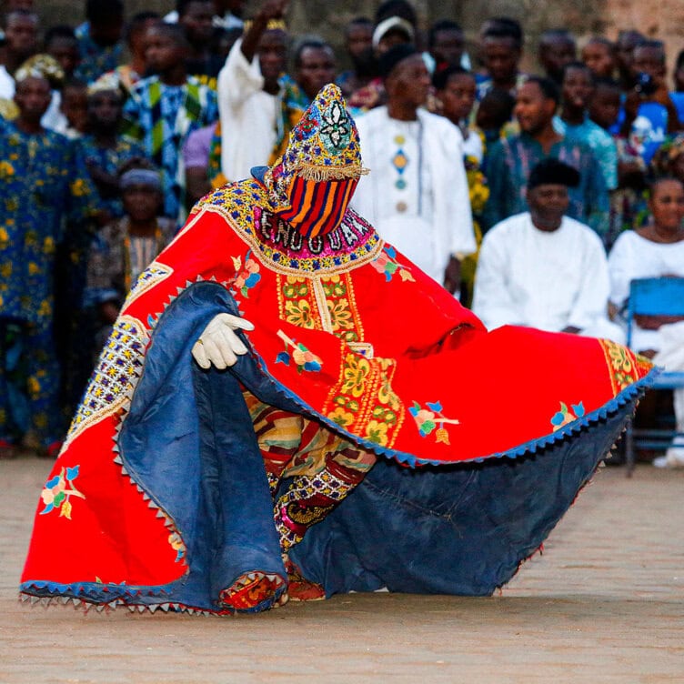 In a vibrant, ornate costume, the performer dazzles the crowd in 2025. The red ensemble with intricate patterns and hood makes this moment not to miss. Spectators clad in colorful attire create an unforgettable backdrop to this mesmerizing scene.