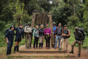 A group of hikers, ready to embark on their adventure, poses before the Kilimanjaro National Park sign at Lemosho Gate, surrounded by dense forest. Perfect for those following a beginner's guide to climbing Mount Kilimanjaro.