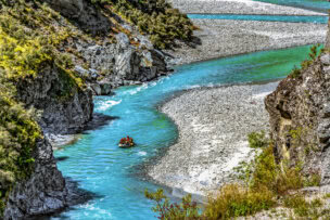 A group of people whitewater rafting down a winding turquoise river in Queenstown, surrounded by rocky cliffs and greenery, is one of the top attractions and thrilling things to do.