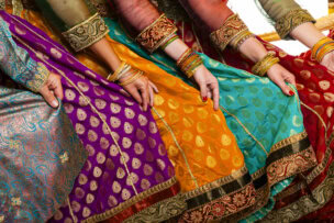 Women in colorful traditional dresses with intricate patterns hold their flowing skirts along the bustling streets of Varanasi. They wear matching bangles on their wrists, adding to the vibrant tapestry of India's cultural heritage.