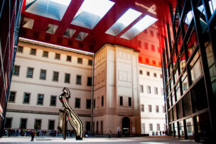 A tall, modern sculpture stands in the courtyard of a Madrid building with large red ceiling panels, blending historical and contemporary architecture—a must-see for anyone exploring travel destinations and things to do in this vibrant city.